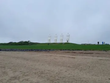 The Man by the Sea sculpture with four large white seated figures on a grassy mound above a sandy beach.
