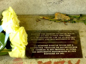 Protective plaque on Oscar Wilde\'s tomb with yellow roses beside it.