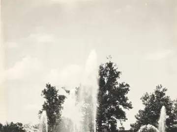 Two women walk past the Swann Memorial Fountain with water jets spraying into the air.