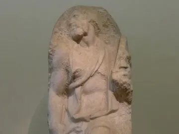Unfinished marble sculpture of Saint Matthew emerging from stone, with a bearded figure looking upward.