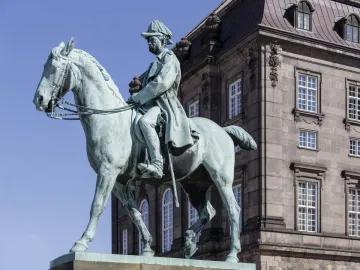 Christian IX equestrian statue in bronze against a blue sky, with a building facade behind it.
