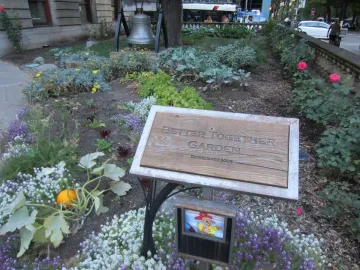 The Liberty Bell mounted in a garden bed beside a stone building and flowering plants.
