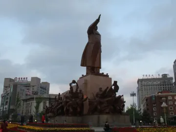 The Long Live the Victory of Mao Zedong Thought statue in a city square, with Mao raising an arm on a tall pedestal and smaller bronze figures around the base.