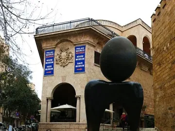 Monument a la dona by Joan Miró, a dark abstract sculpture with a sphere on a curved base in front of a historic stone building.