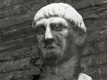 Weathered stone bust of Abbot Luigi with a serious expression, set against a dark brick background.
