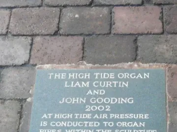 Greenish-blue High Tide Organ information plaque set into brick pavement.