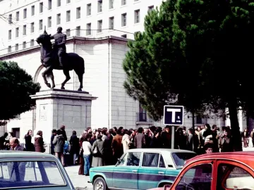 Equestrian Statue of Francisco Franco on a tall stone pedestal in an urban square with trees, cars, and a crowd nearby.