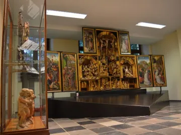 The Fisenne Altarpiece with gilded sculptural reliefs and painted side panels on a dark display stand.