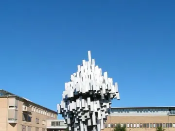 Norra skenet sculpture with white rectangular forms rising on a green lawn near campus buildings