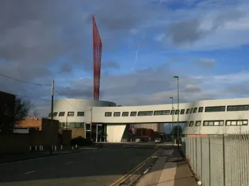 Aspire, a tall red sculpture, rises above a modern curved white building against a partly cloudy blue sky.