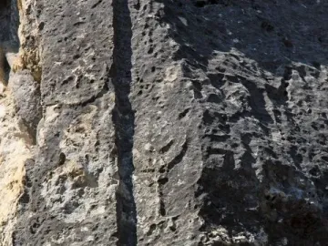 Weathered Athena relief carved into a rough stone surface with a vertical groove and faint eroded details.