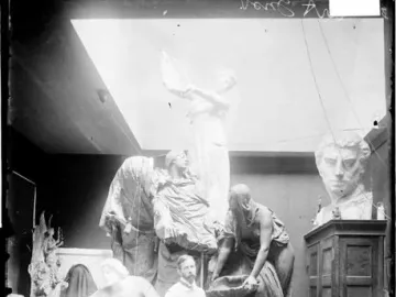 Clay or plaster models of the Fountain of the Great Lakes sculpture group stand in an artist’s studio with a man in an apron among them.