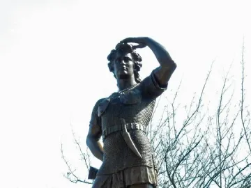 Leif Ericson bronze statue on a pedestal, with one hand raised to his brow against a bright sky.