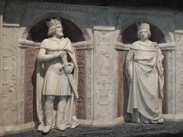 Marble statues of a crowned man holding a sword and a crowned woman in the Tomb of Francis II, set in an ornate carved niche.
