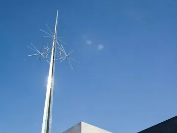 Ad Astra, a towering gold-colored abstract sculpture with star-like elements at the top against a blue sky.