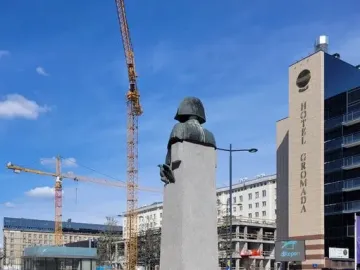 The Emperor Napoleon I Memorial bust on a tall plinth in a gravel plaza, with construction cranes and buildings in the background.