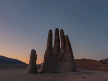 Mano del Desierto rising from a barren desert landscape at dusk with distant mountains on the horizon.