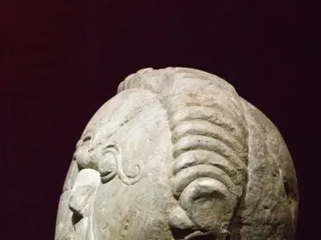 Mšecké Žehrovice Head stone sculpture shown in profile on a black stand, with stylized facial features and ribbed hair bands.