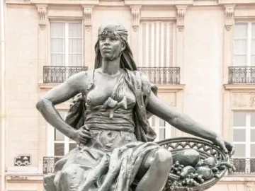 Africa sculpture of a seated woman holding a basket of fruit and vegetables, with her foot resting on a tortoise.