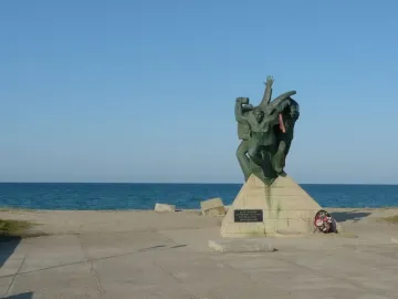 Bronze monument of the Eupatoria Assault showing three dynamic figures on a stone pedestal by the sea.