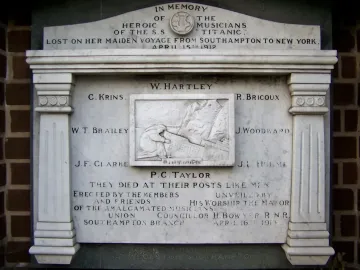 Titanic Musicians\' Memorial plaque with a central mourning figure and engraved names on a brick wall.