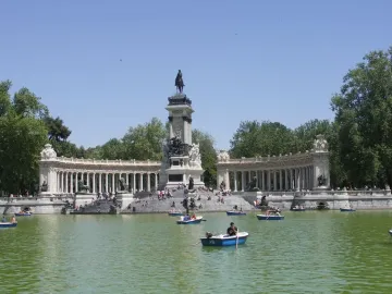 The Alfonso XII Monument with a central equestrian statue, flanked by curved colonnades beside a lake with rowboats.