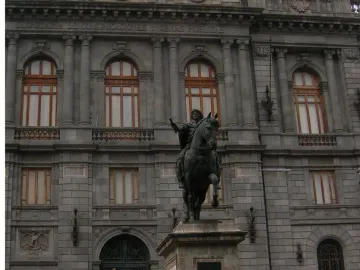 El Caballito, a dark equestrian statue on a stone pedestal, with a grand stone building in the background.
