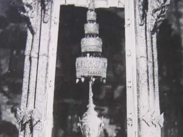 Emerald Buddha statue seated in meditation beneath an ornate shrine and hanging ornament.