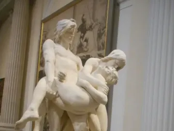 The First Funeral marble sculpture showing three figures, with two adults carrying a limp smaller figure between them.