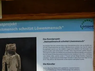 The Lion-man sculpture, a tall light-colored wooden figure with a human body and animal-like head beside an information board.