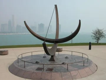 Man Enters the Cosmos sundial sculpture on a circular granite base with Chicago skyline and boats in the background.