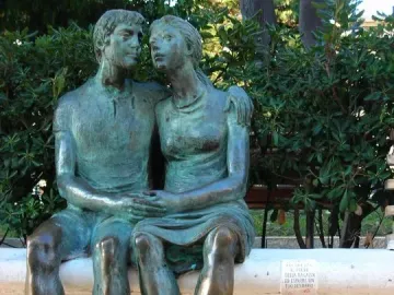The Muretto of Alassio bronze sculpture of a seated man and woman embracing on a decorated stone wall