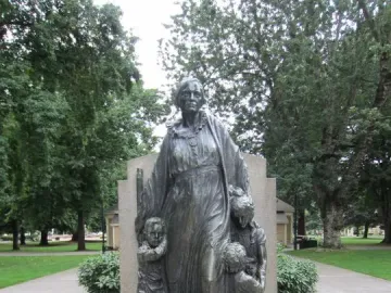 Pioneer Mother Memorial sculpture showing a standing figure with three children on a rocky base in a park setting.
