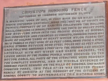 Bronze commemorative plaque for Running Fence mounted on a reddish-brown wall.