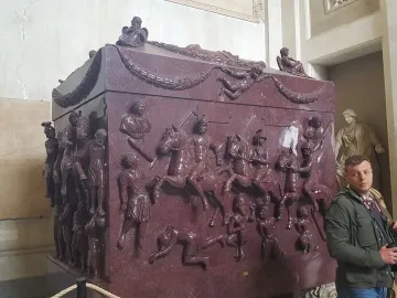 Sarcophagus of Helena with high-relief battle scenes of horsemen and foot soldiers in a museum gallery.