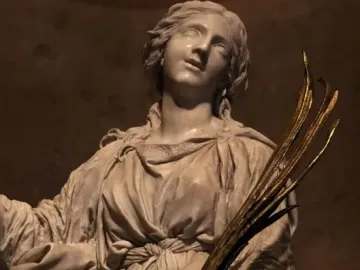 Marble sculpture of St Bibiana looking upward, holding a bundle of golden branches.