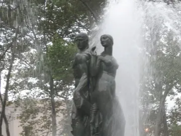 Bailey Fountain with a dark metallic man and woman standing back to back on a stone pedestal amid water sprays.