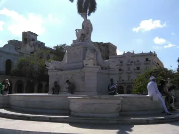 Fuente de la India marble fountain with a crowned female statue and fish sculptures at the base in a sunny plaza