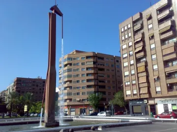 The Pink Panther sculpture fountain in a concrete plaza with apartment buildings and parked cars nearby.