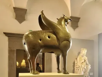 Bronze Pisa Griffin statue on a pedestal in a museum gallery.