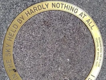 Circular brass commemorative plaque for the Skylon embedded in grey pebbled ground.