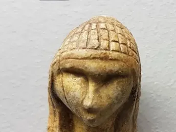 Replica of the Venus of Brassempouy showing a small stylized human head with a prominent nose and patterned hair or headdress.