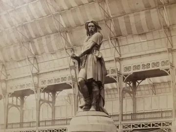 The Vercingetorix monument stands on a stepped circular pedestal inside a large glass-roofed exhibition hall.