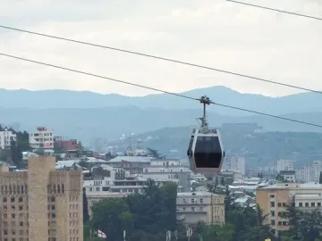 Freedom Monument rises above the Tbilisi skyline beneath gondola lift cables.