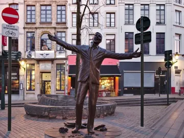 The Jacques Brel memorial bronze statue stands on a circular platform in a cobblestone square, with outstretched arms and a microphone stand nearby.