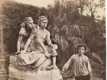 Kanaris brothers monument with two classical male figures in a garden, with a young man standing beside it