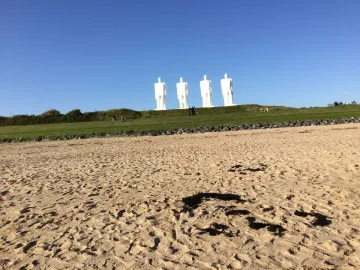 The Man by the Sea sculpture on a grassy hill above a sandy beach, with several visitors nearby.