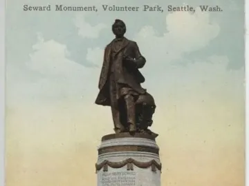 William Henry Seward bronze statue on a stone pedestal in a park, with trees and gravestones in the background.