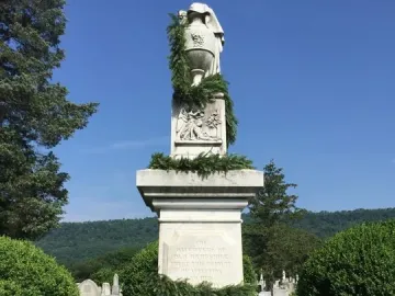 Confederate Memorial stone monument with an urn on top, garlands, and small Confederate flags around the base.