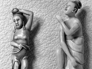 Two carved female figures, one standing with raised arms and one kneeling with a tilted-back head.